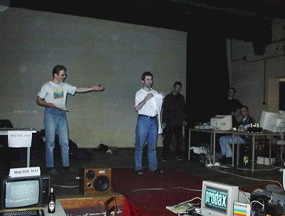 Wotnau - the coferencier on the left. Raster receiving another T-Shirt for his great Atari demo called Self Demo. Speccy organisers in the background. (both from Czech Republic)